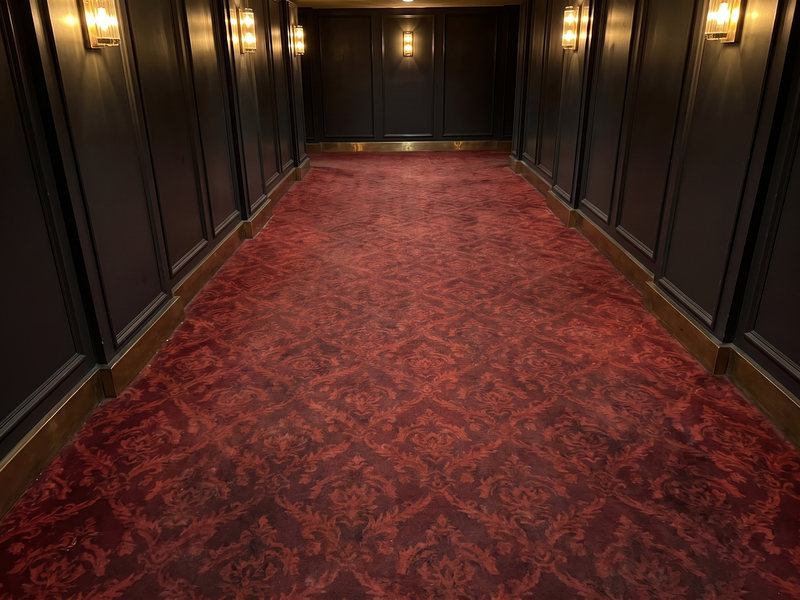The same theater lobby carpet after hot-water extraction cleaning, the red damask pattern restored to an even, deep color with the pile lifted
