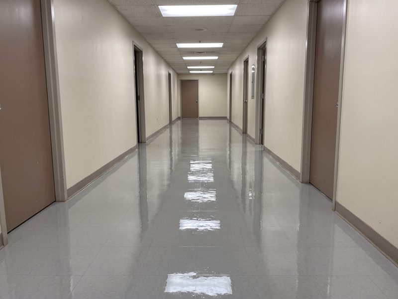 The same corridor floor after stripping, waxing and burnishing, with a high-gloss finish reflecting the ceiling lights