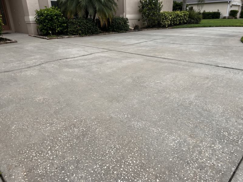 The same concrete driveway after power washing, back to clean, evenly colored light gray concrete